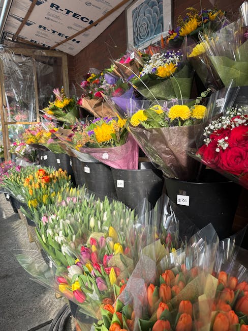 An indoor flower shop showcasing an assortment of fresh floral bouquets arranged in large black tubs and smaller containers. The display includes vibrant tulips in shades of orange, pink, yellow, and 